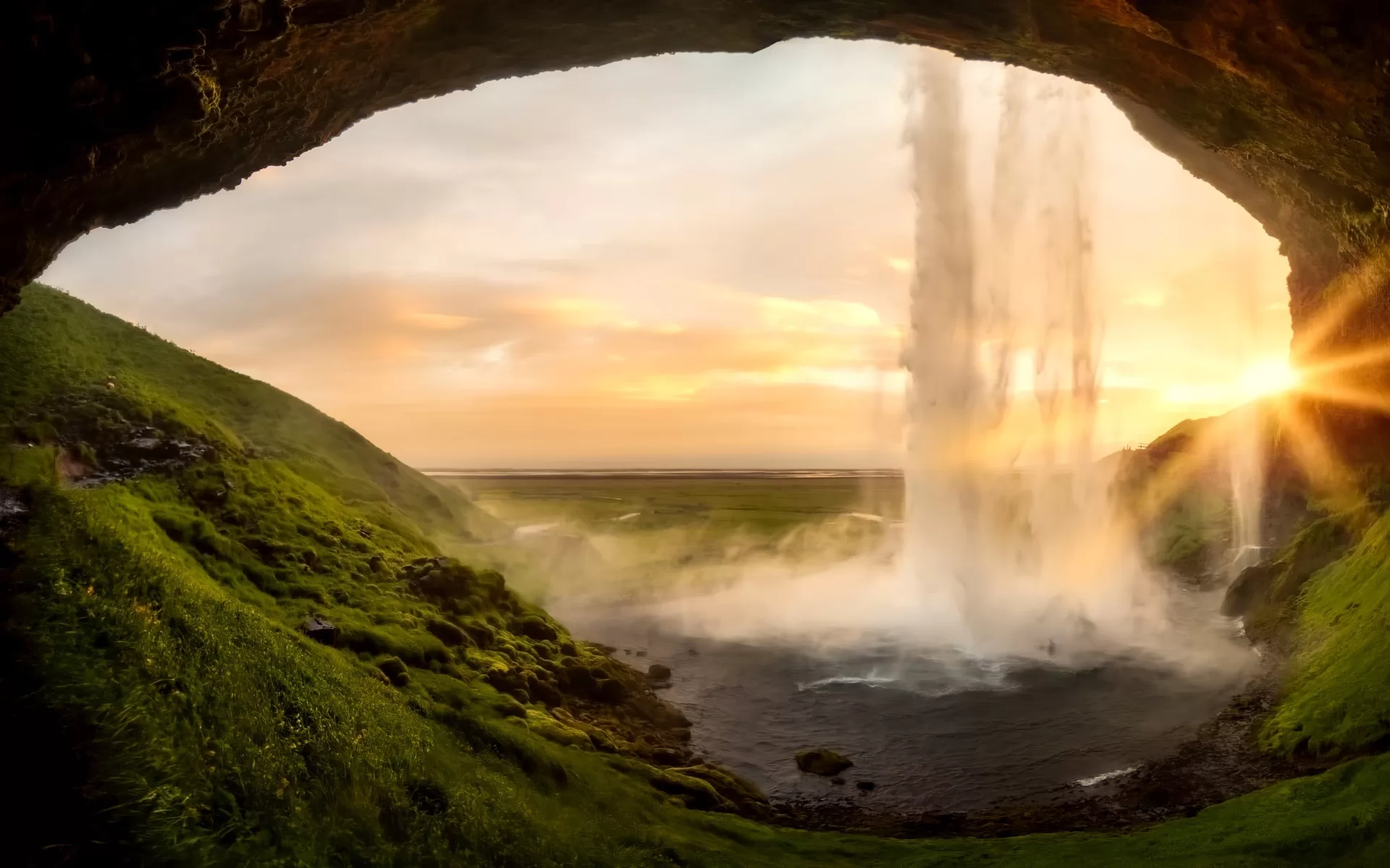Een waterval voor een grot tijdens een zonsondergang in IJsland