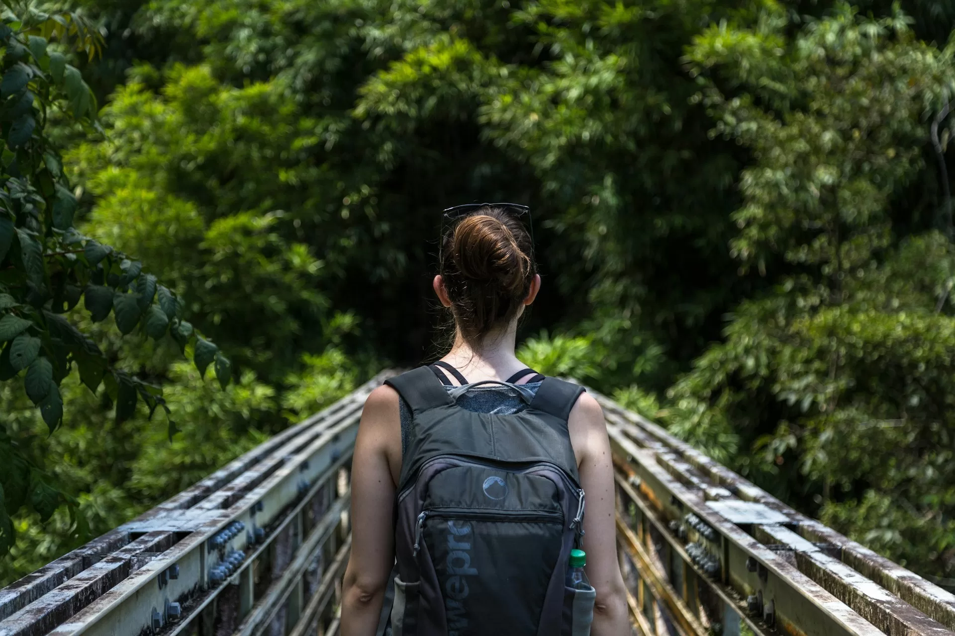Vrouw loopt over stalen brug in Pipiwai Trail, Hana Maui Hawaii, met tropisch groen op de achtergrond