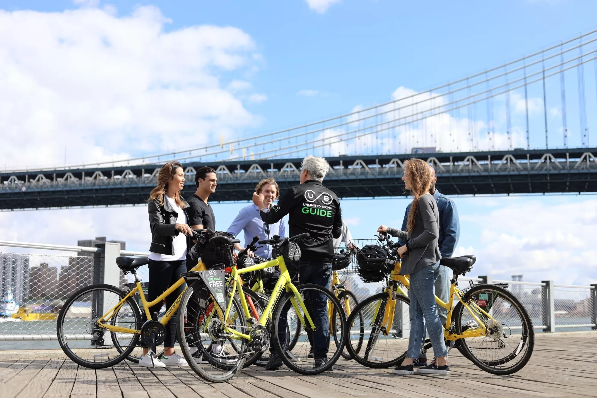 Vijf mensen met gids fietsen op gele fietsen, tijdens fietstour bij Brooklyn Bridge, zonnige dag