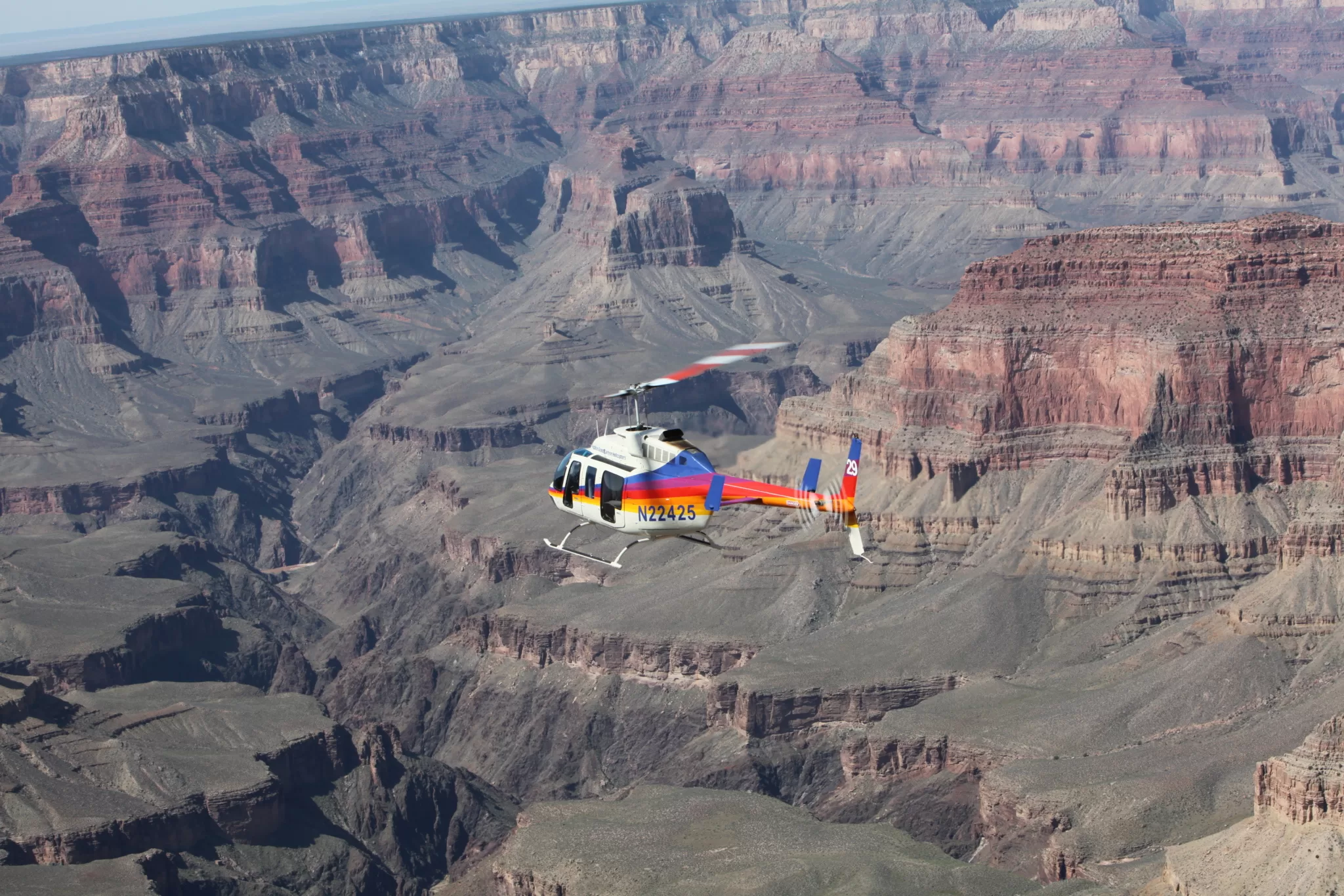 Kleurrijke helikopter vliegt boven de Grand Canyon, luchtfoto met zicht op diepe kloven en rotsformaties