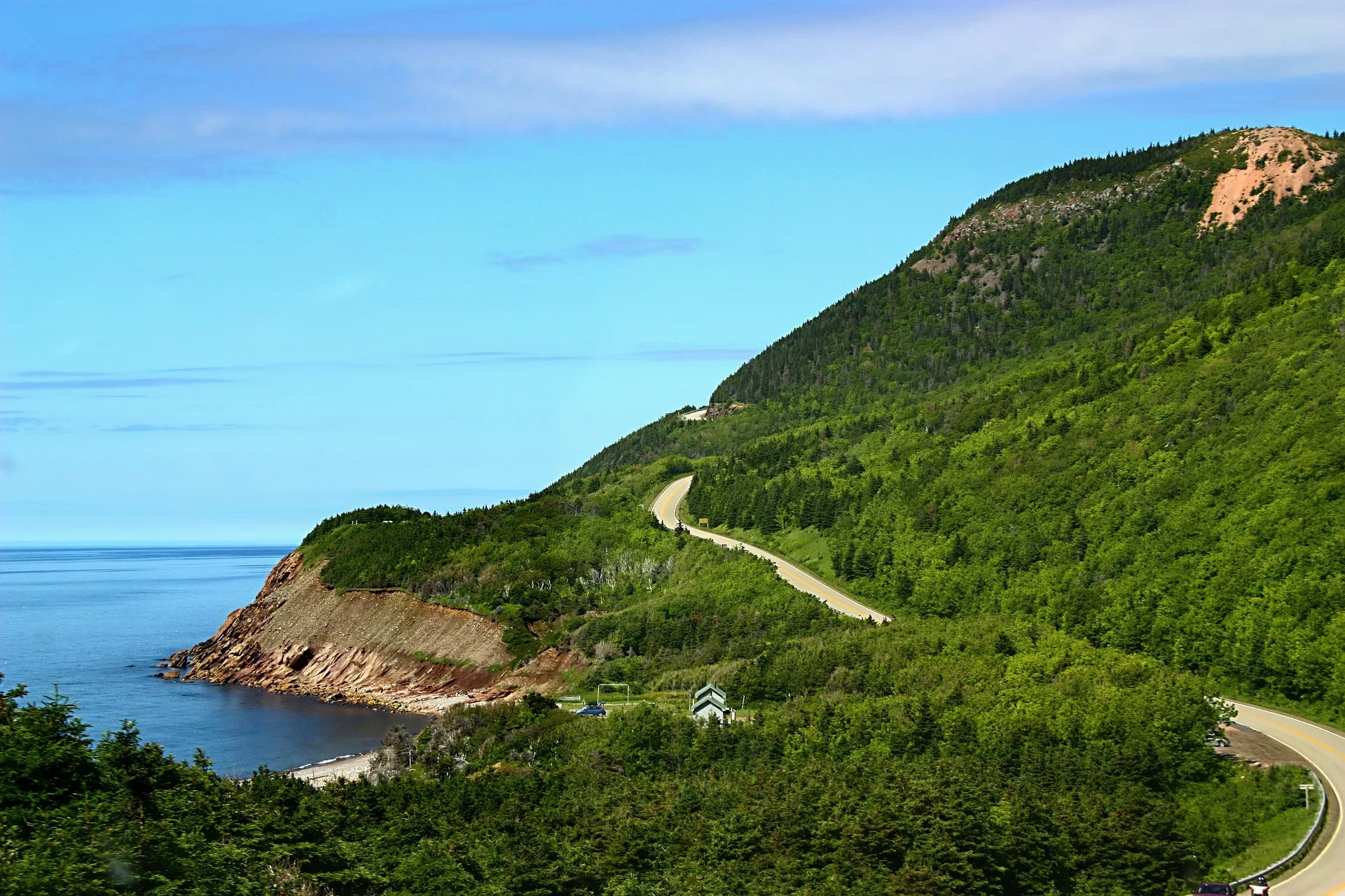 Slingerende weg tussen de goene bomen van Cape Breton met de Atlantische Oceaan op de achtergrond