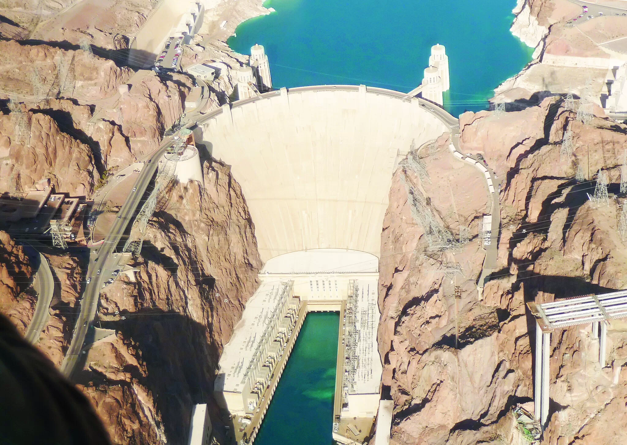 Luchtfoto van de Hoover Dam tussen rode rotsen, met turkoois waterreservoir en infrastructuur rondom de dam.