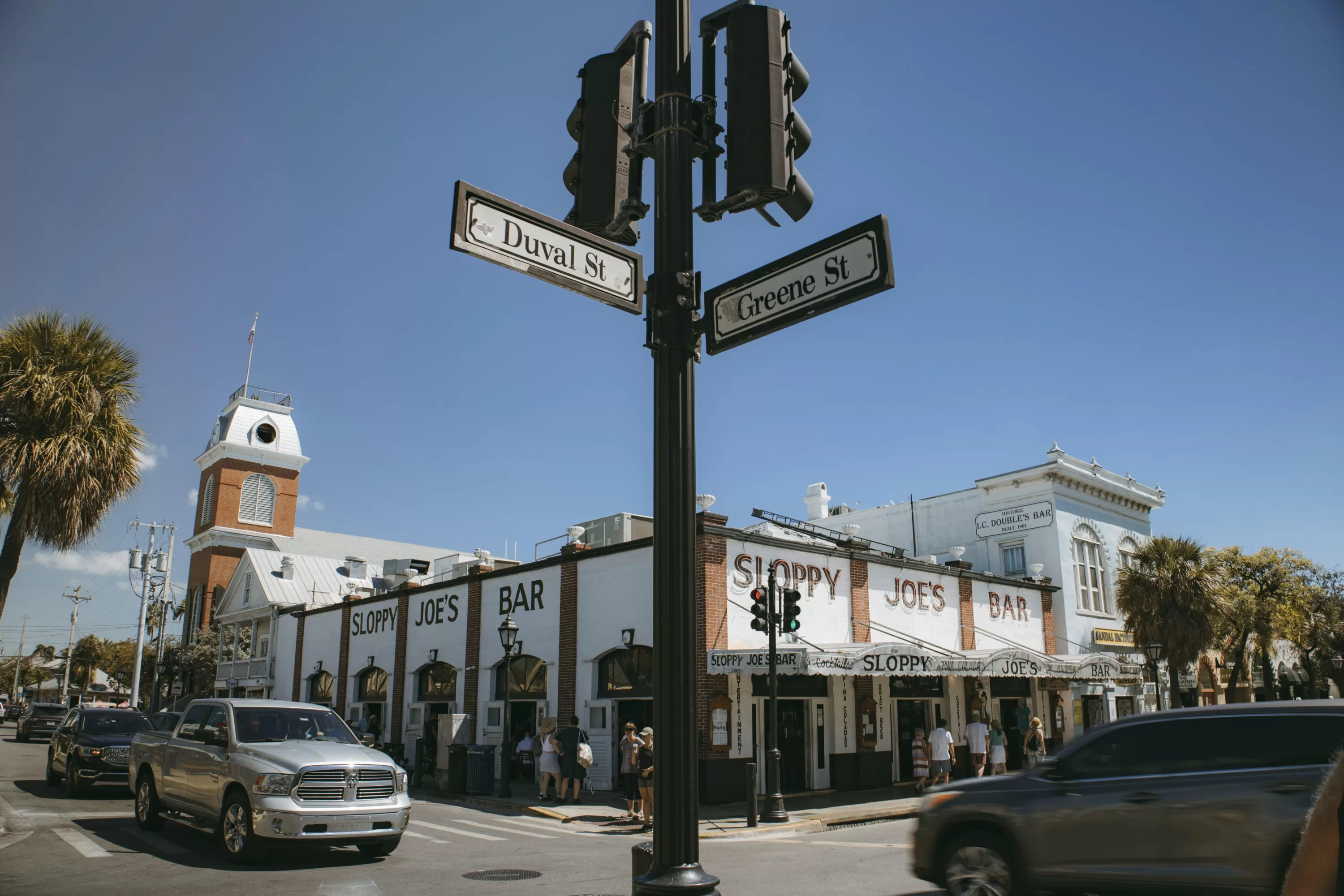 Straßenecke Duval St und Greene St mit Sloppy Joe's Bar und vorbeifahrenden Autos in Key West an einem sonnigen Tag