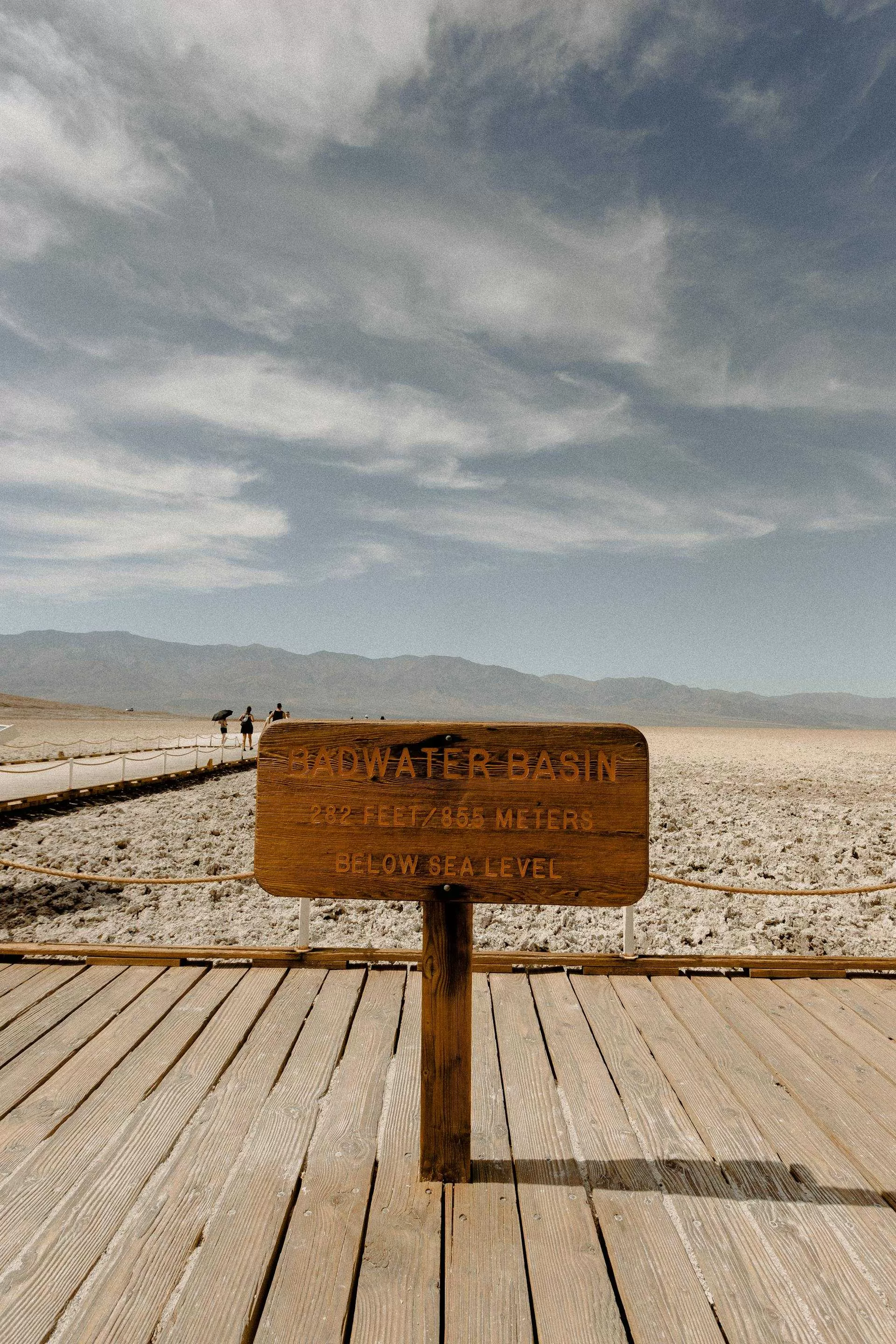 Houten bord bij Badwater Basin in Death Valley, 282 voet onder zeeniveau, droog zoutlandschap en wandelpad zichtbaar