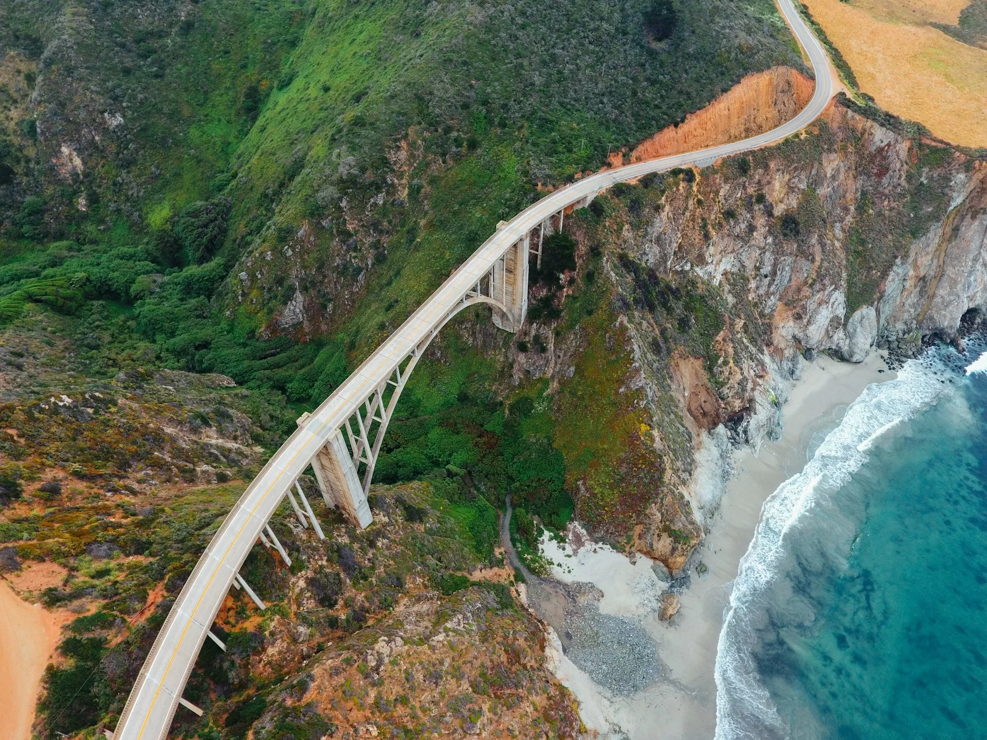 Bixby Creek Bridge in Californië, gezien vanuit de lucht, met de kustlijn en groene heuvels op de achtergrond