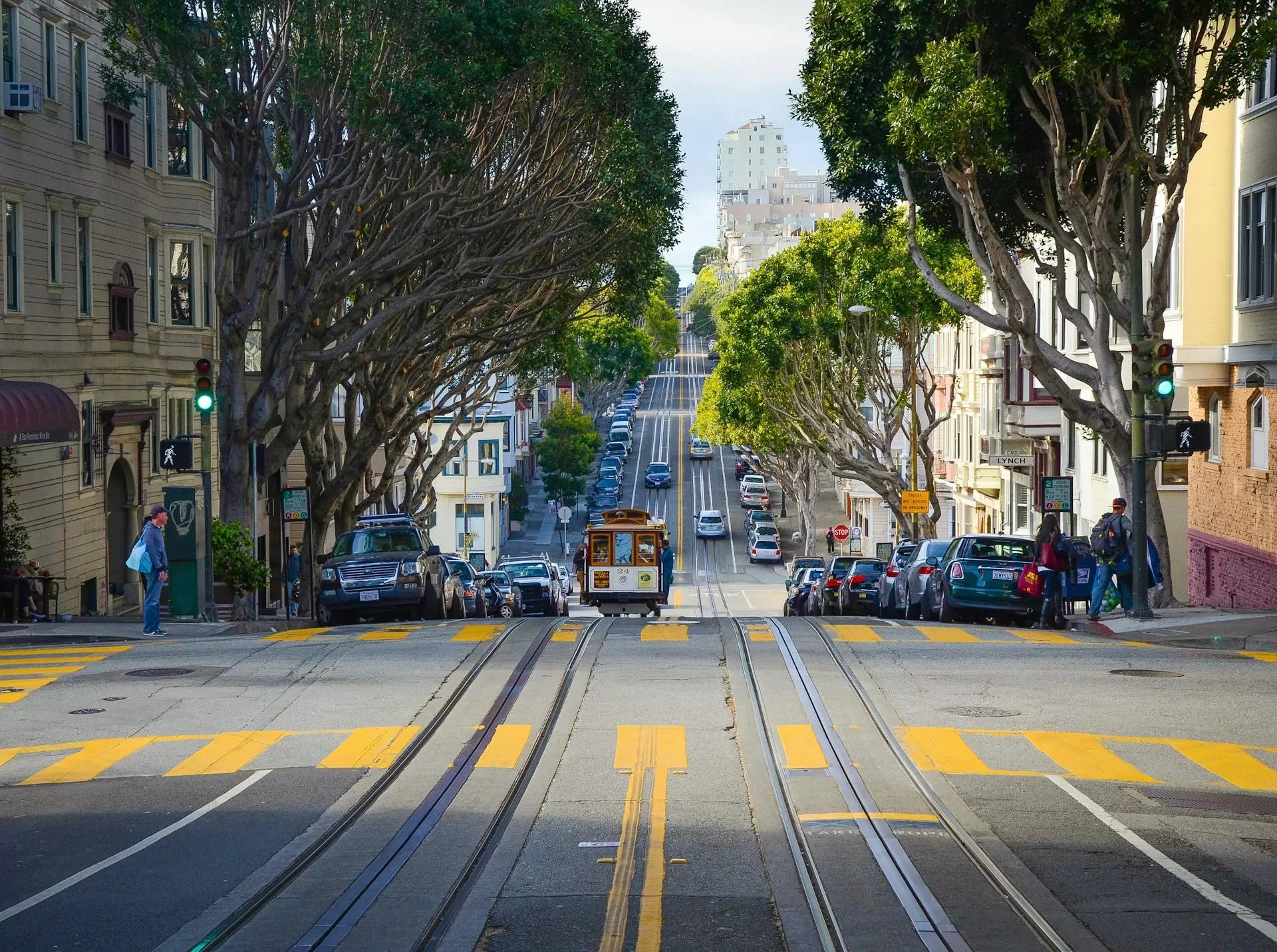 Traditionele tram rijdt over brede straat in San Francisco, omringd door auto's en stedelijke architectuur.