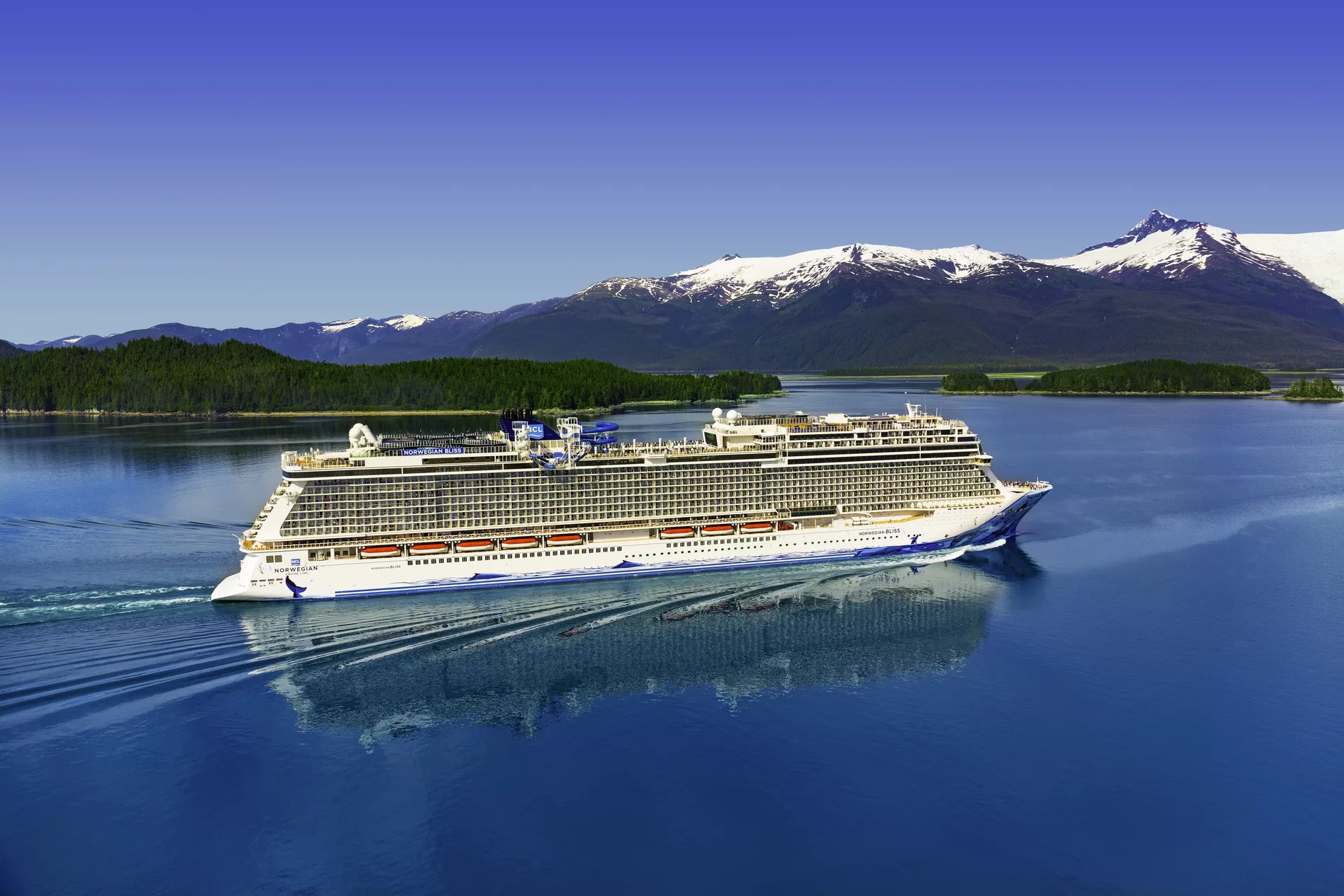 De Norwegian Jewel varend door de wateren van Alaska met besneeuwde bergtoppen op de achtergrond.