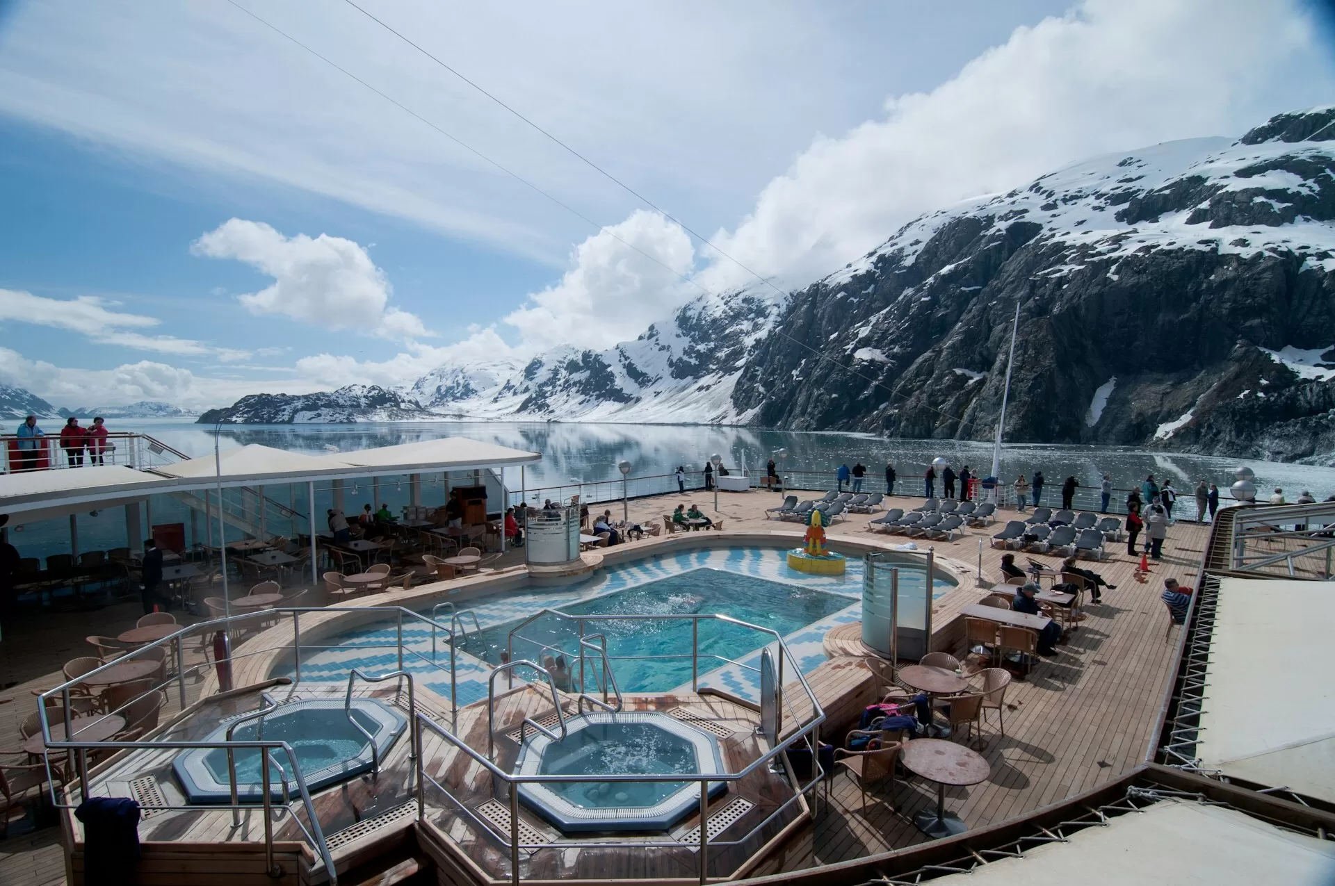 Mensen op het zwembaddek van een Norwegian cruiseschip varend door een besneeuwd Glacier Bay