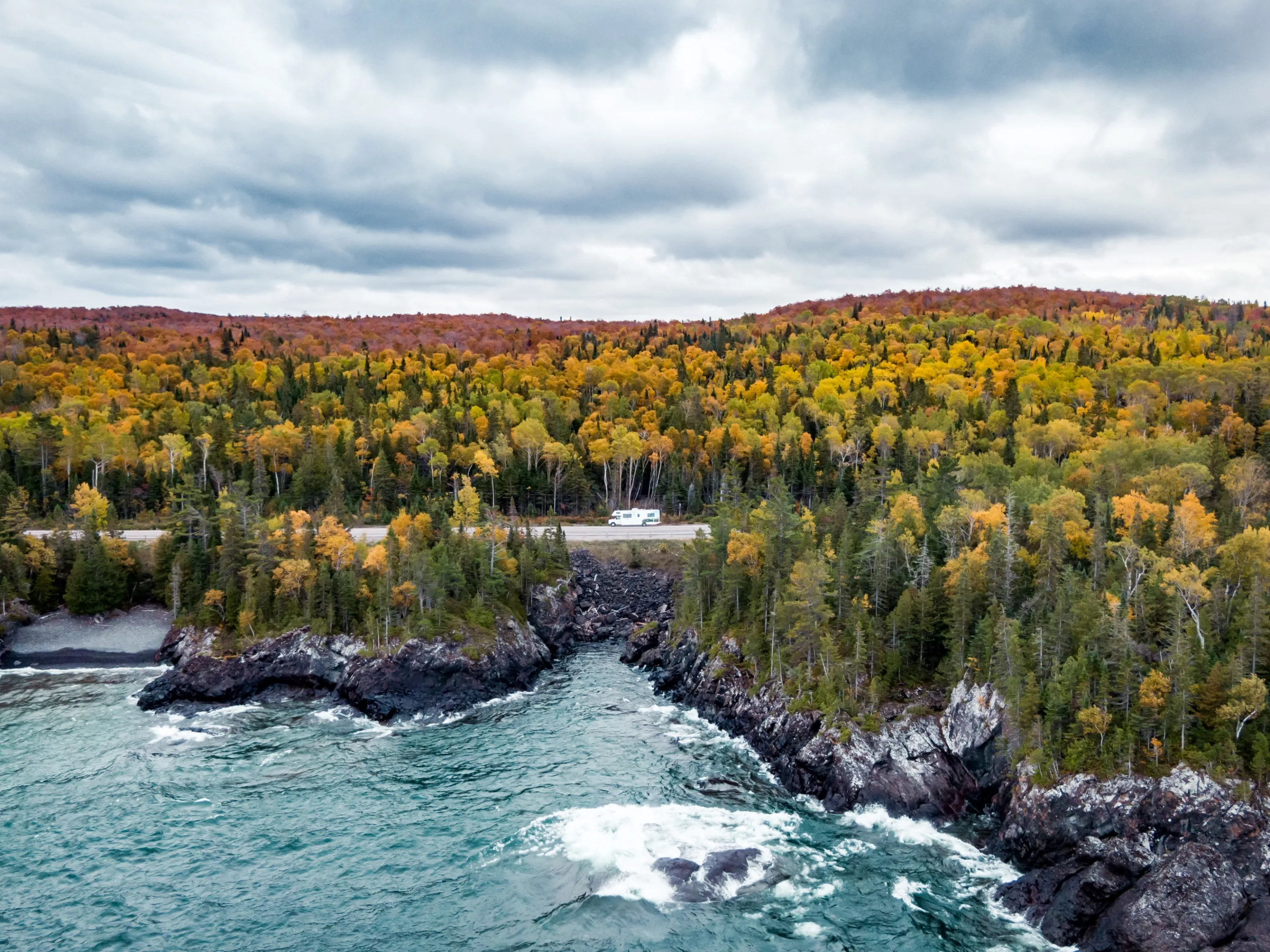 Camper rijdt langs de kustweg, omringd door bos met uitzicht op de oceaan