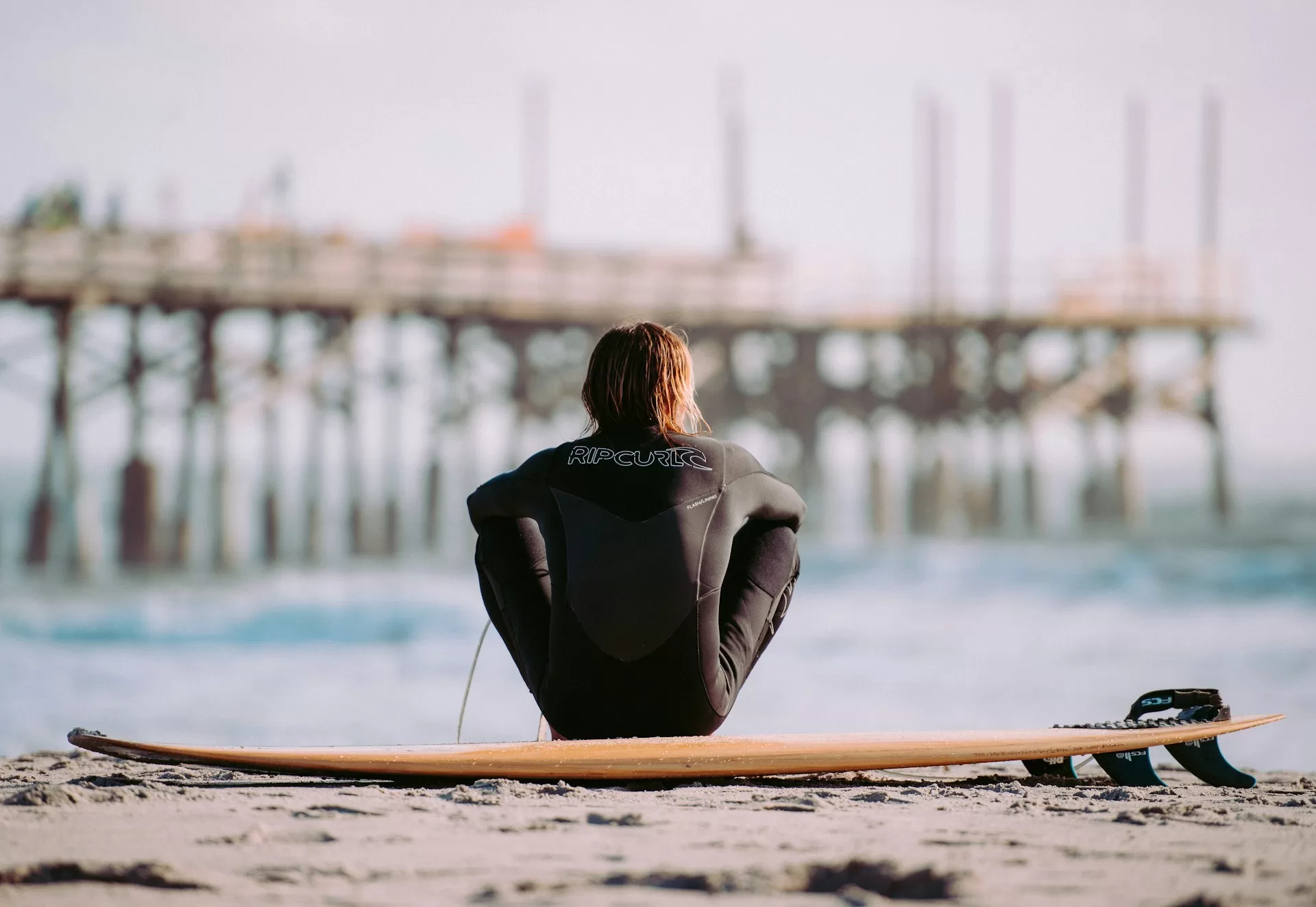 Surfer zit op het strand van Cocoa Beach voor de pier