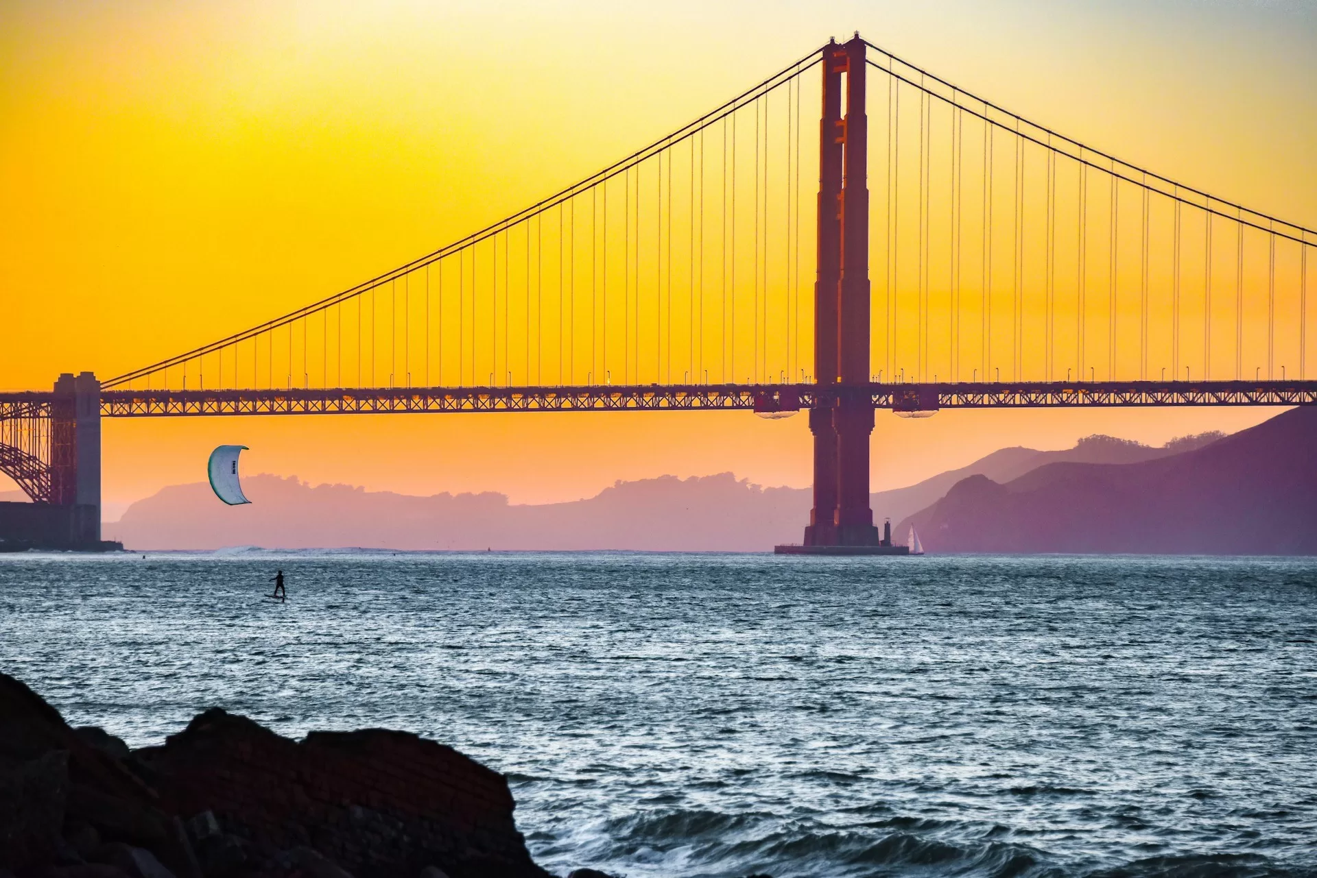 Golden Gate Bridge met windsurfer bij oranje-gele lucht tijdens zonsondergang