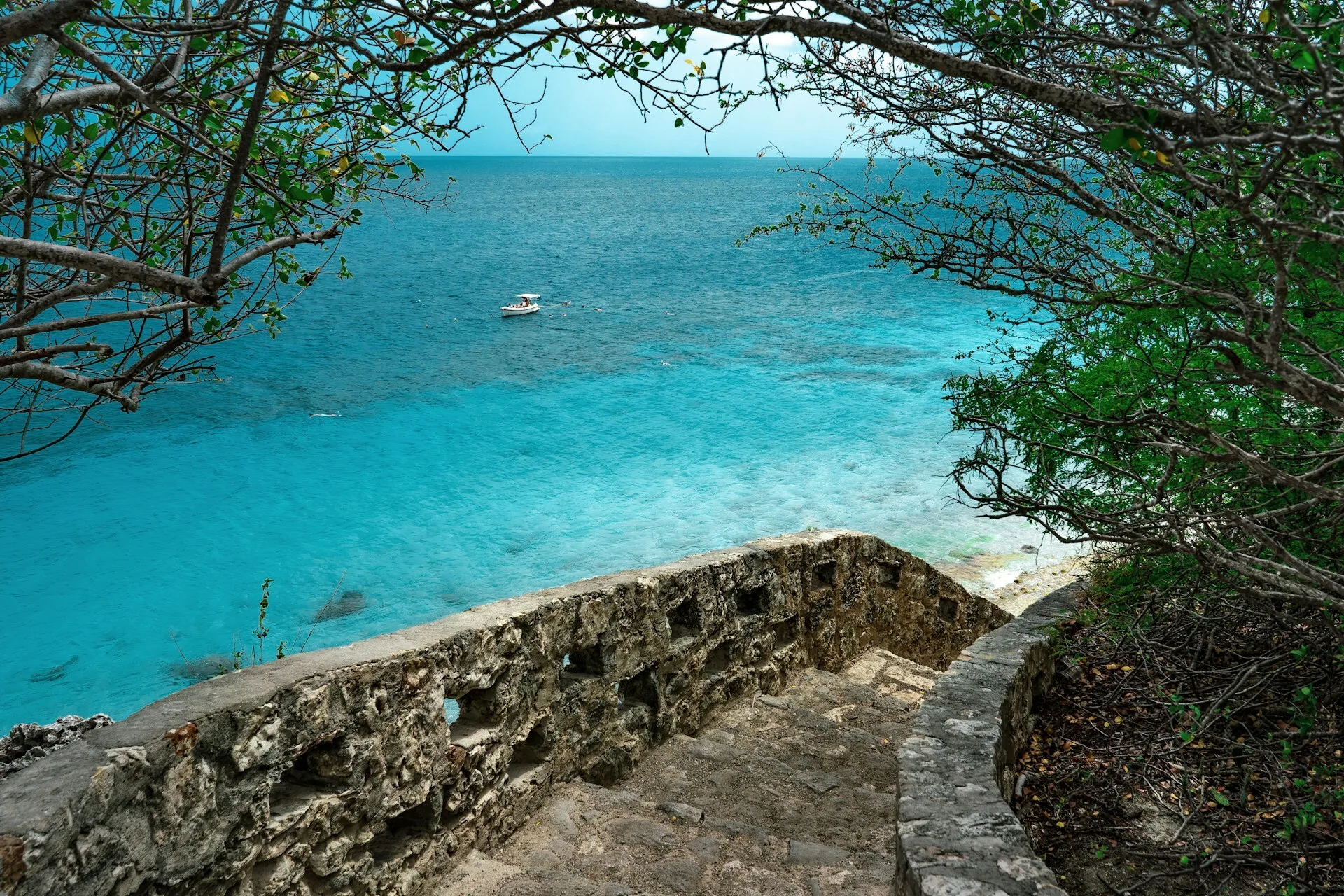Een stenen trap die leidt naar een klein strand met helderblauw water op de achtergrond op Bonaire