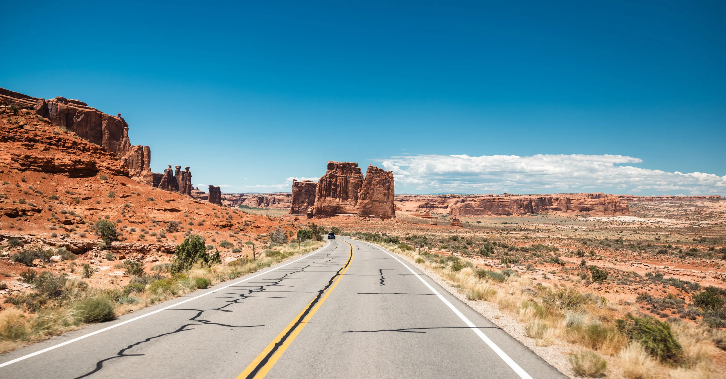 Monument Valley met een weg en rotsformaties in de verte, omgeven door uitgestrekte landschappen