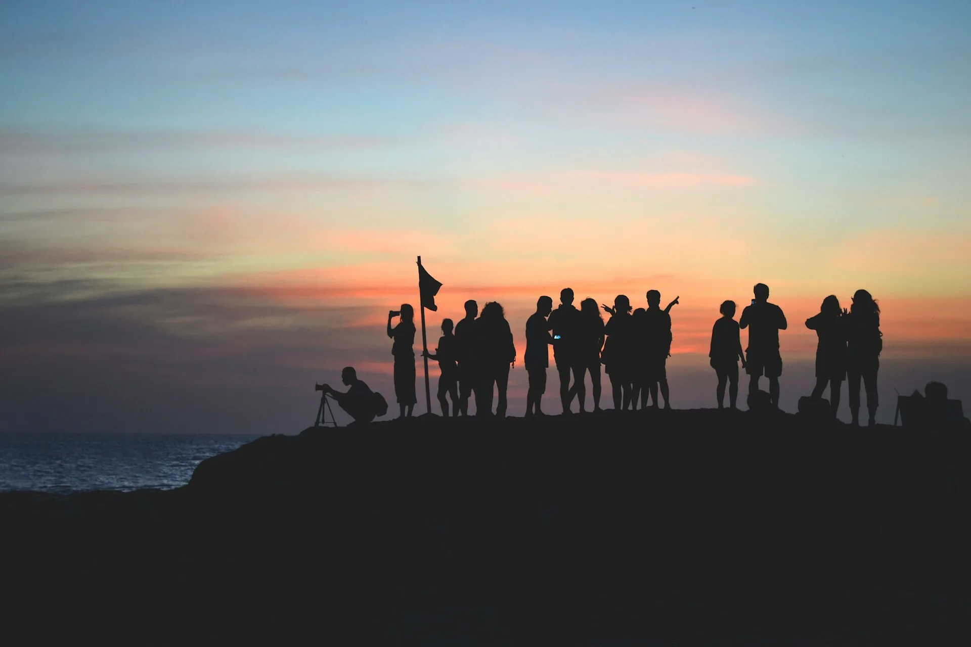 een groep mensen op een berg aan de kust, terwijl ze naar de zonsondergang kijken