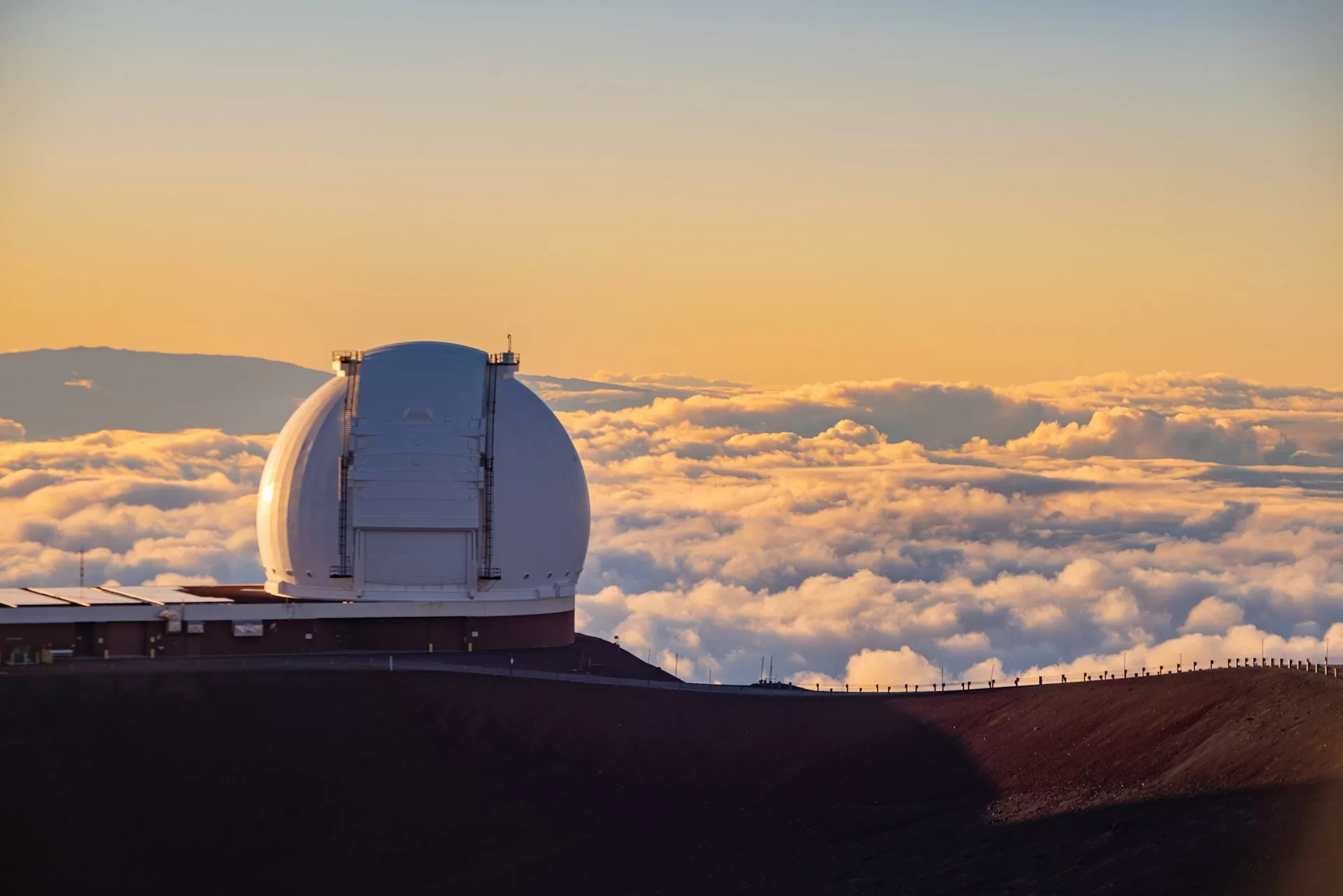 Mauna Kea met wolken bij zonsondergang, bergtop verlicht door gouden zonlicht