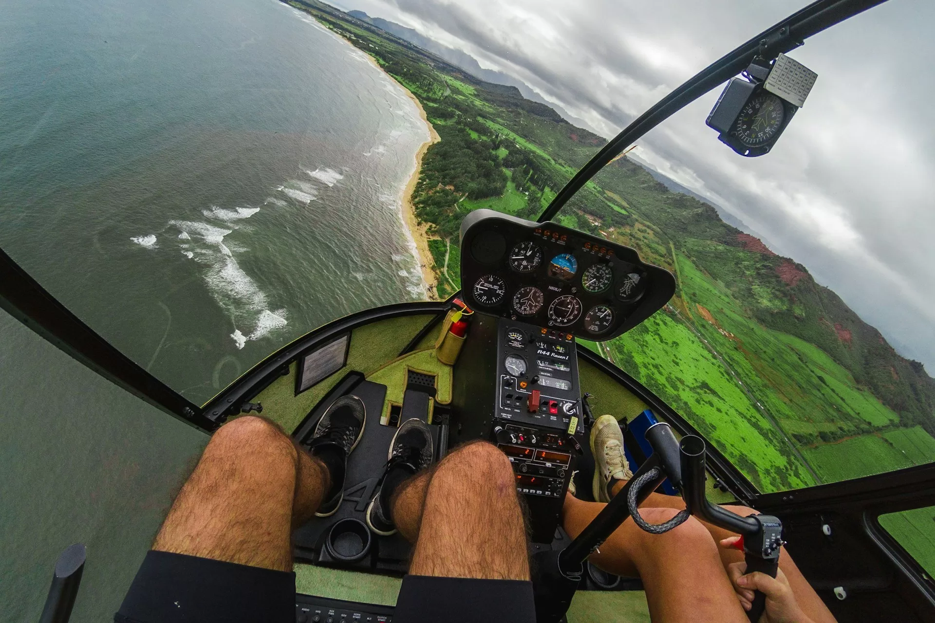 Twee mensen in een helikopter met uitzicht over de zee en het groene landschap van Kauai, Hawaï