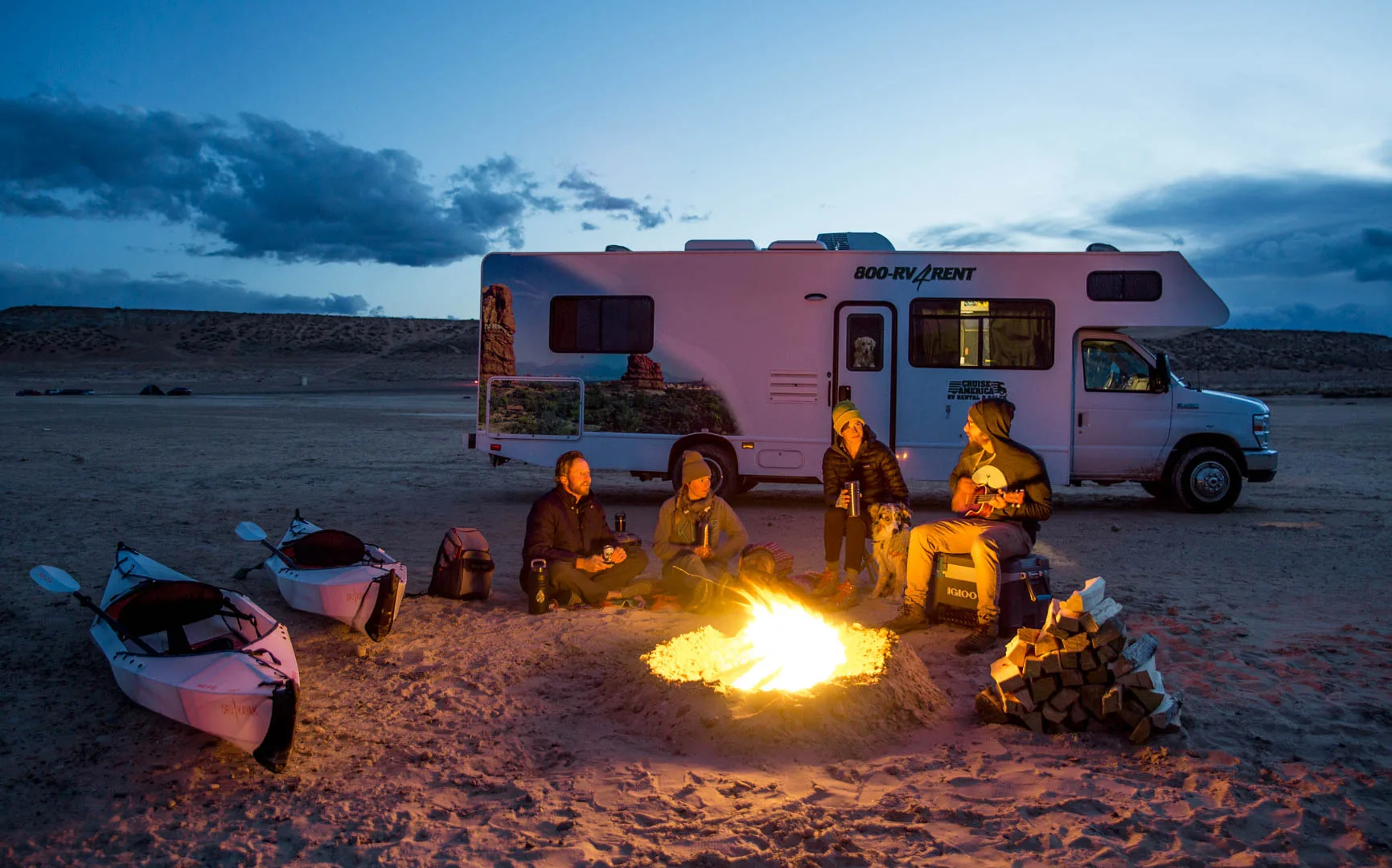 Een Cruise America camper op een strand met mensen om een kampvuur
