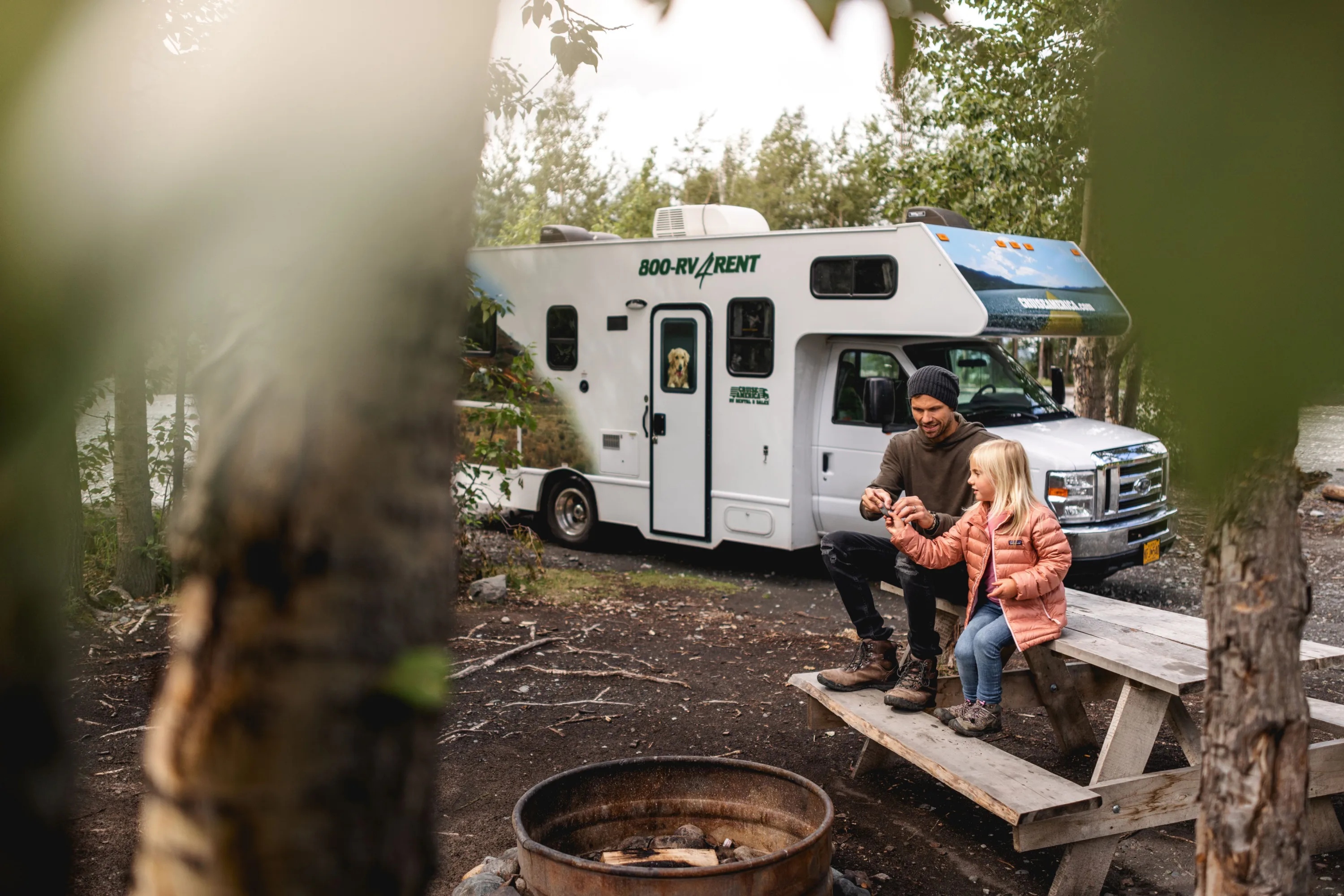 Een Cruise America camper tussen de bomen met vader en dochter