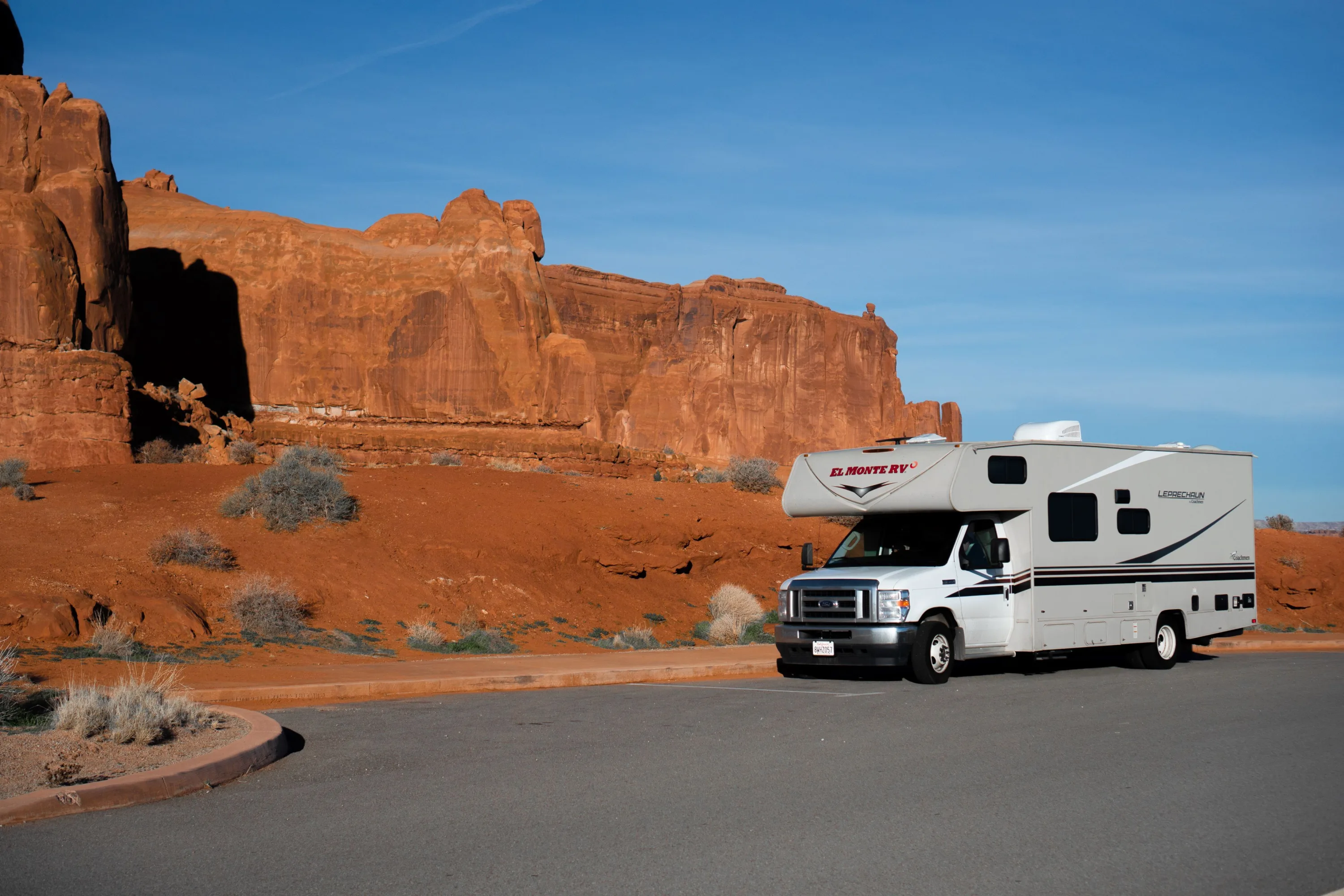 Een El Monte camper op een weg langs rode rotsformaties