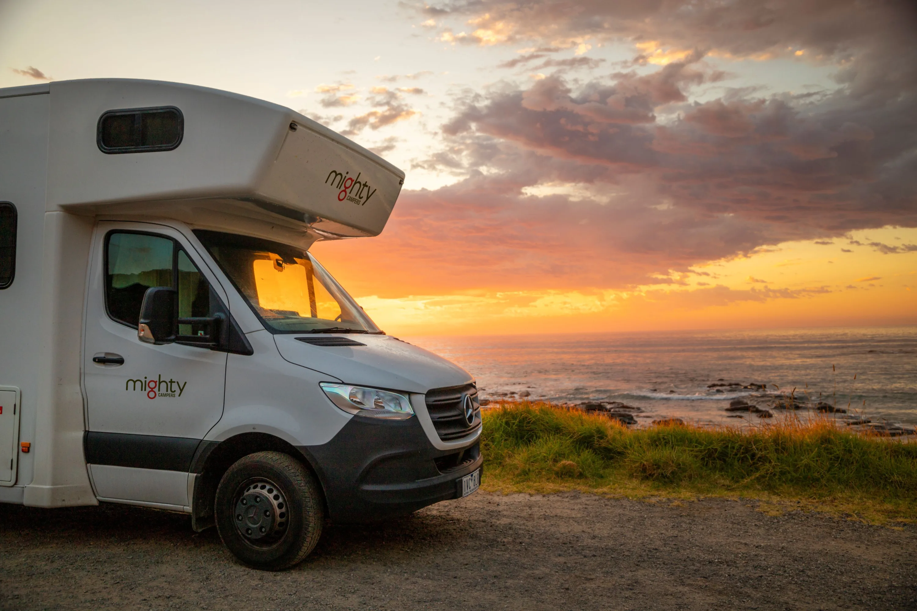Een Mighty camper op een weg langs de kust tijdens een zonsondergang