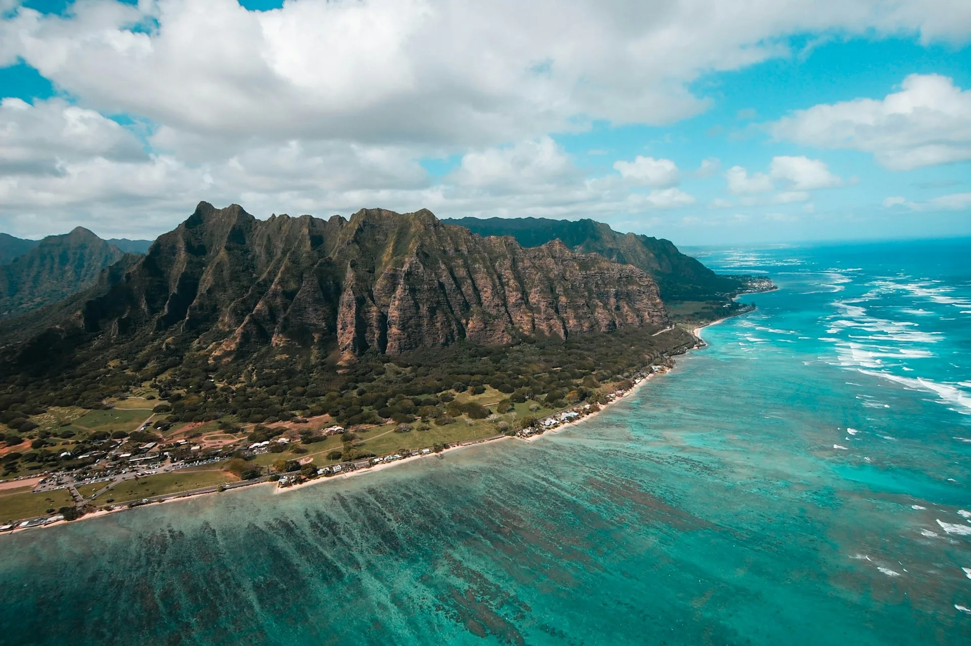 Luchtfoto van Oahu, Hawaii, met groen begroeide rotsen, oceaan op de voorgrond en een dorp in de verte