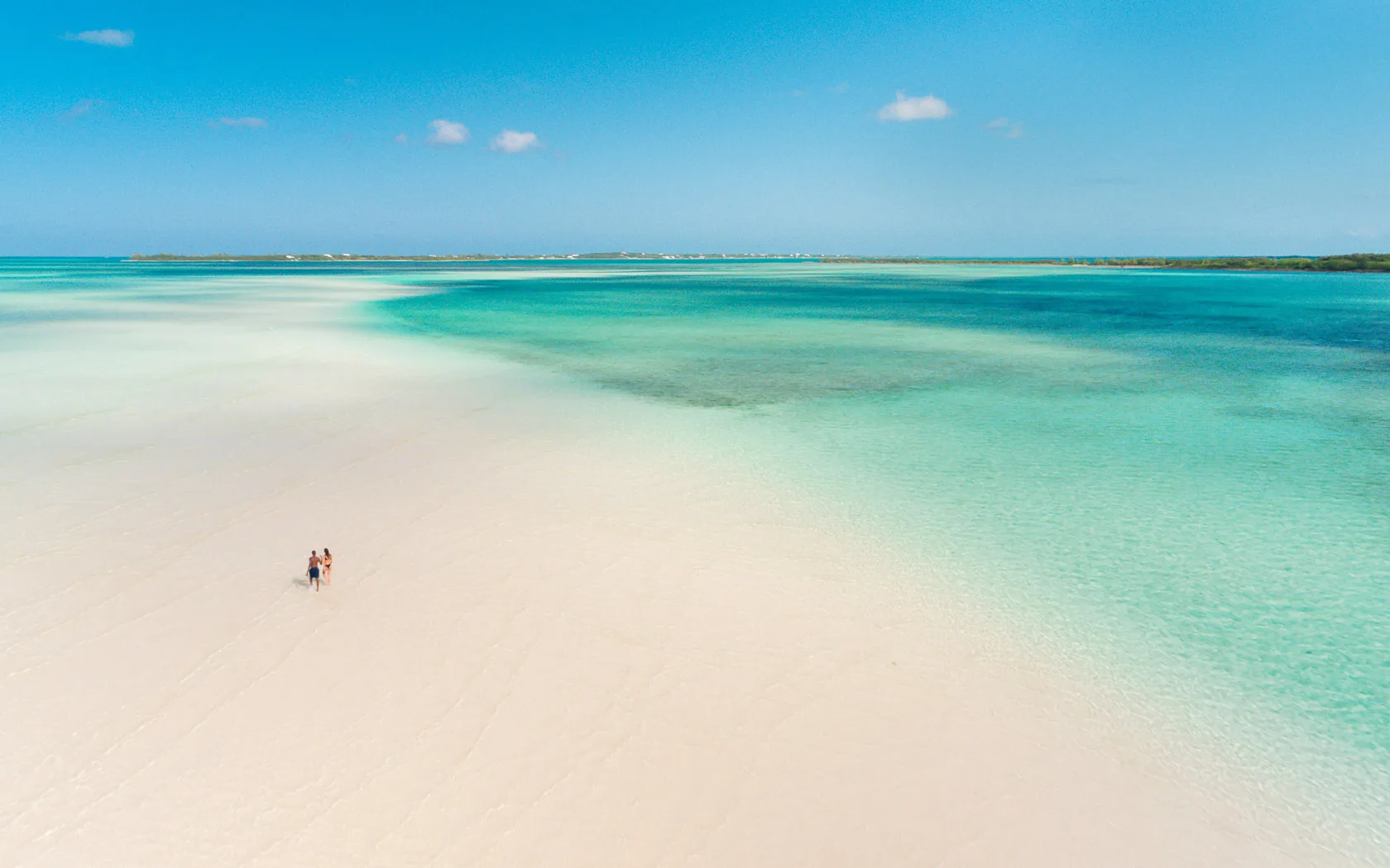 Luchtfoto van een stelletje wandelend op een verlaten en uitgestrekt strand van de Bahama's omringd door azuurblauw zeewater.