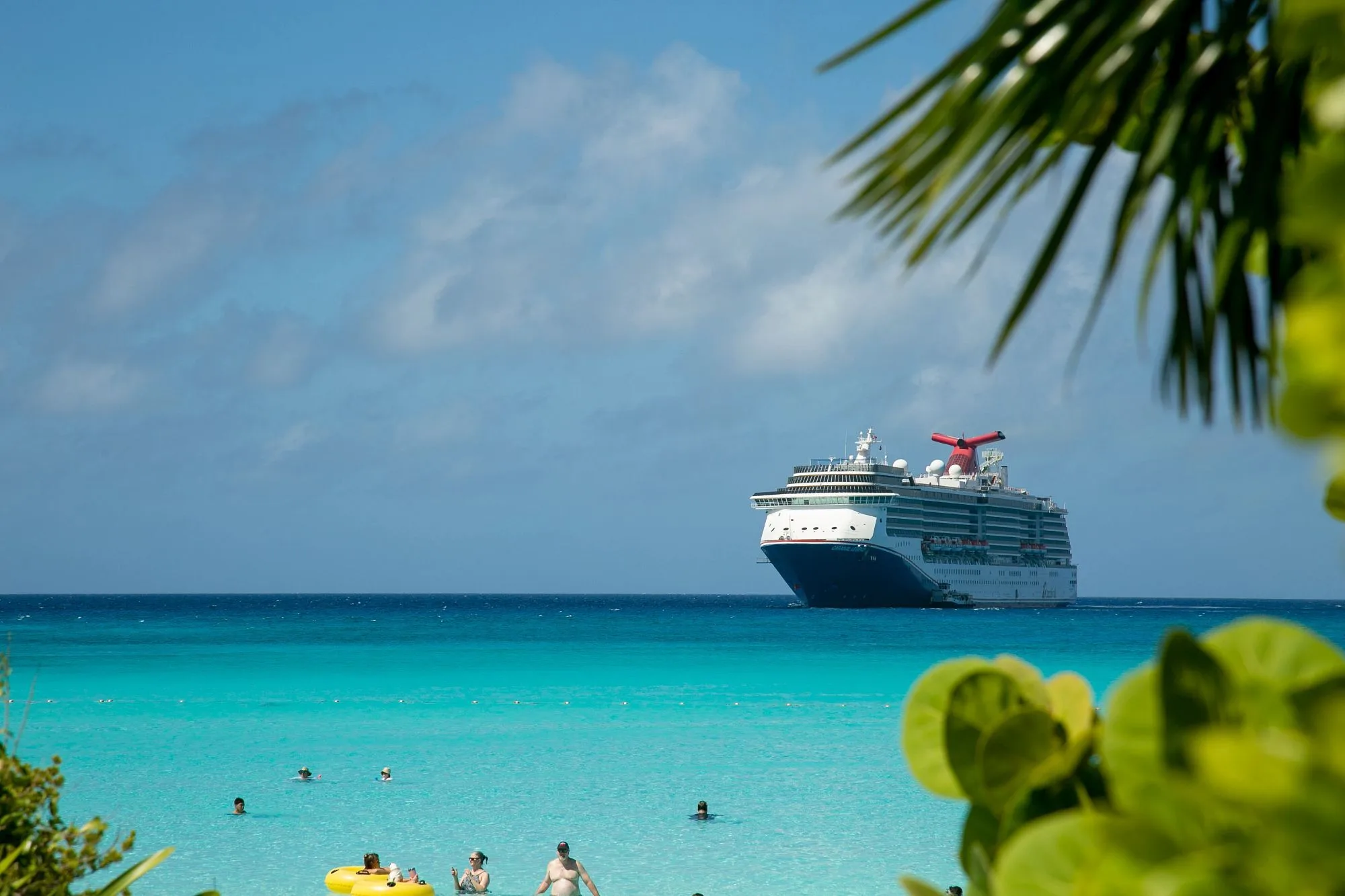Mensen in het azuurblauwe water van de Bahama's met op de achtergrond een cruiseschip op zee