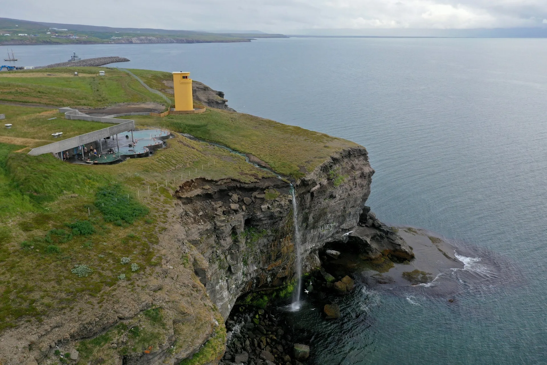 Een spa op een klif met een waterval die de zee in loopt in Húsavík, IJsland
