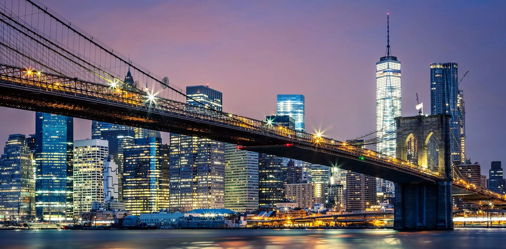 De verlichte skyline van Manhattan New York met de Brooklyn Bridge op de voorgrond.