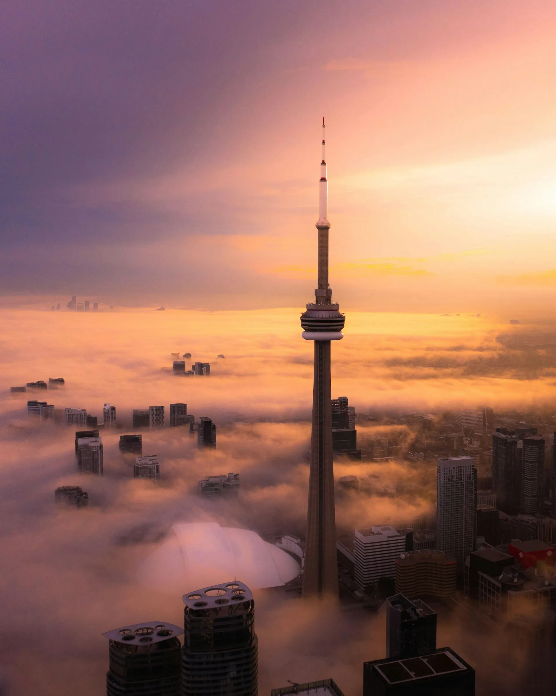 Het hoogste punt van de CN Tower bij zonsondergang en wolkendek onder het uitkijkpunt