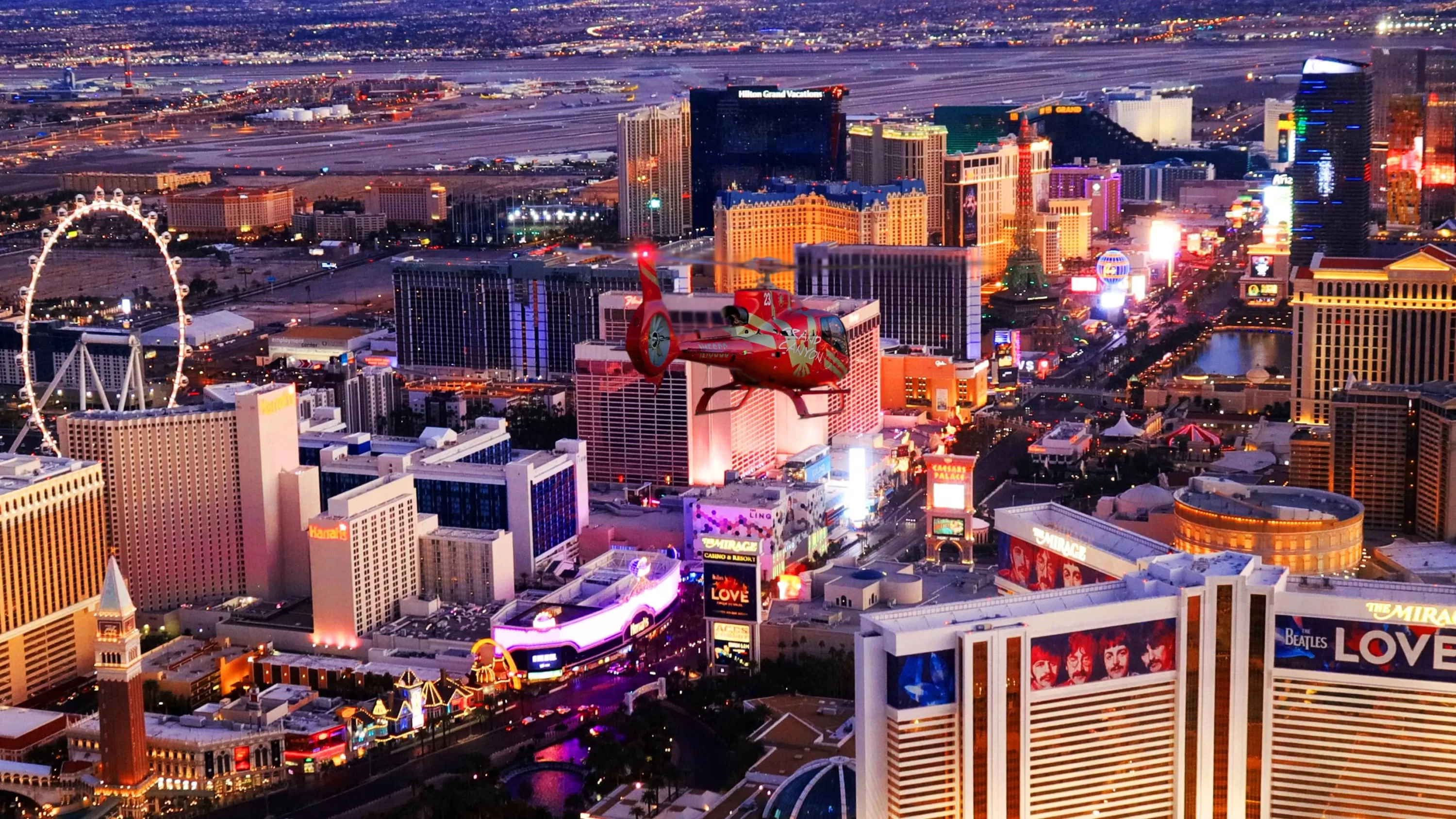 Rood-gouden helikopter vliegt bij zonsondergang over de Strip in Las Vegas met mini-Eiffeltoren en London Eye zichtbaar