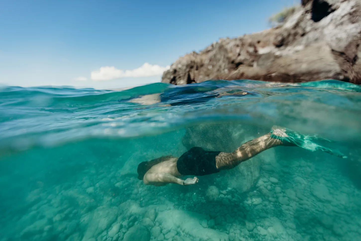 Persoon die onderwater zwemt, foto genomen half in en half uit het water