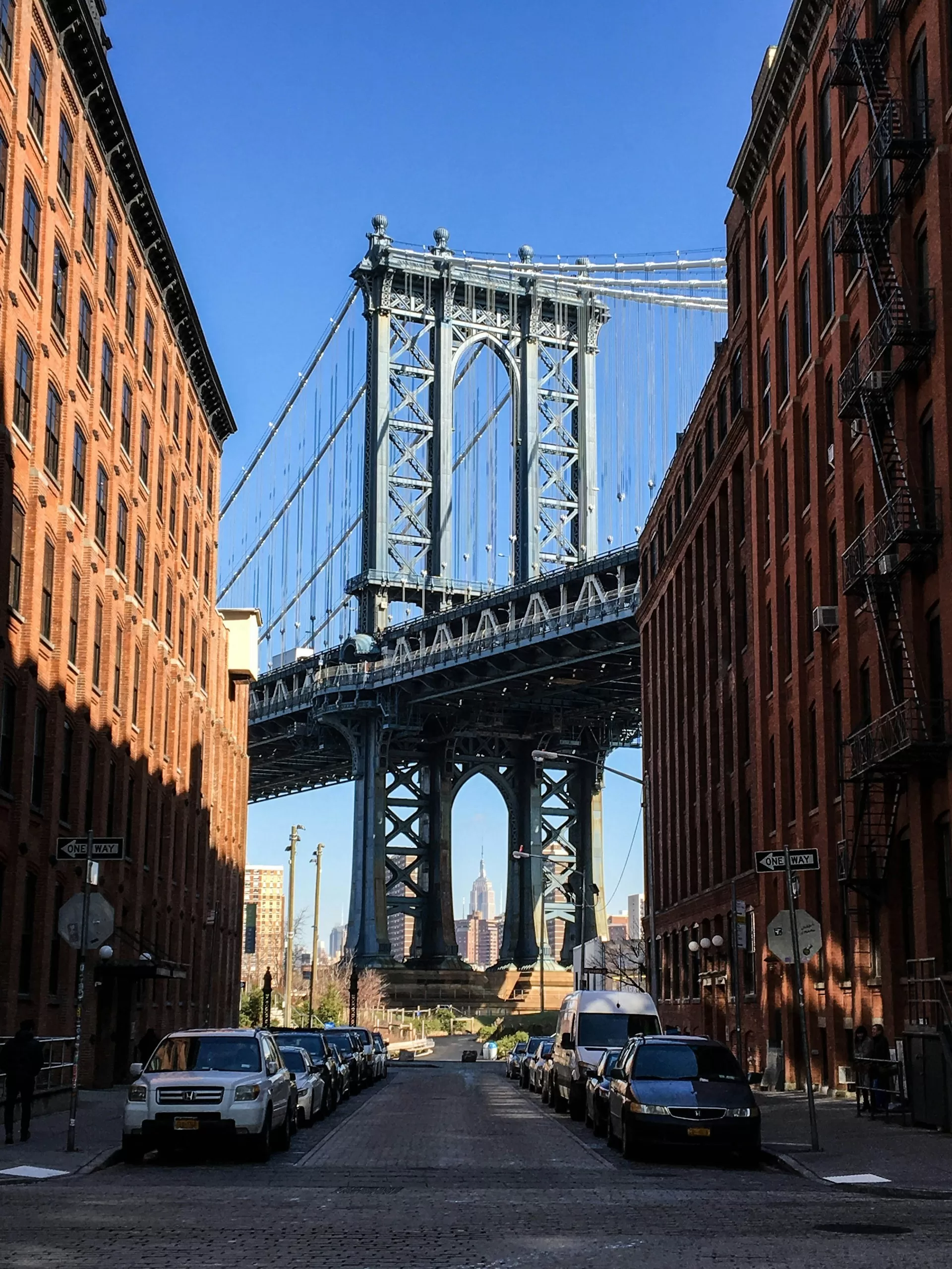 De Manhattan Bridge in New York City vanuit een straat met rode gevels en de blauwe lucht op de achtergrond