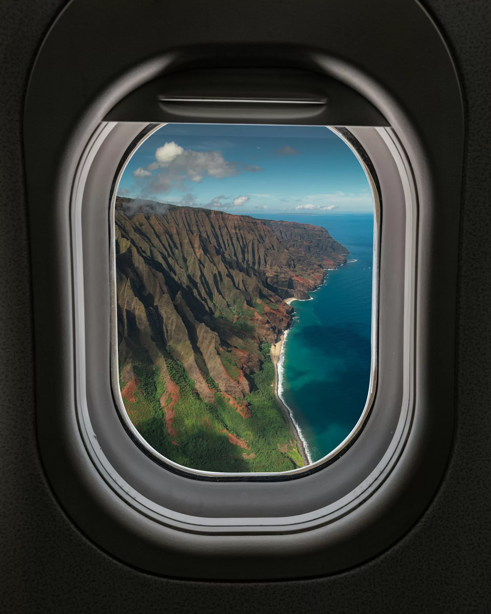 Uitzicht door een vliegtuigraampje over de kust van Kauai