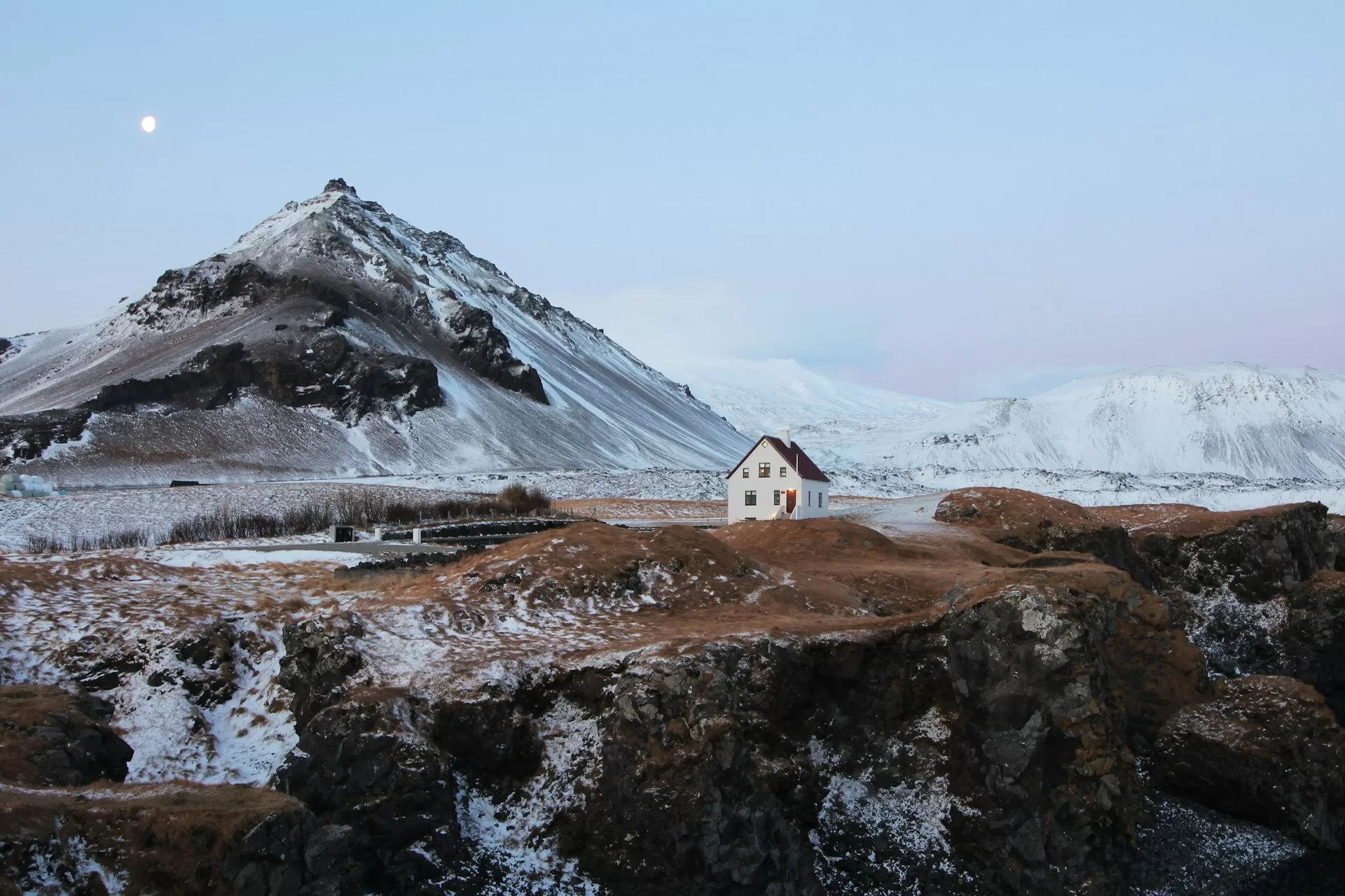 Een huisje tussen de besneeuwde heuvels in Arnarstapi, IJsland