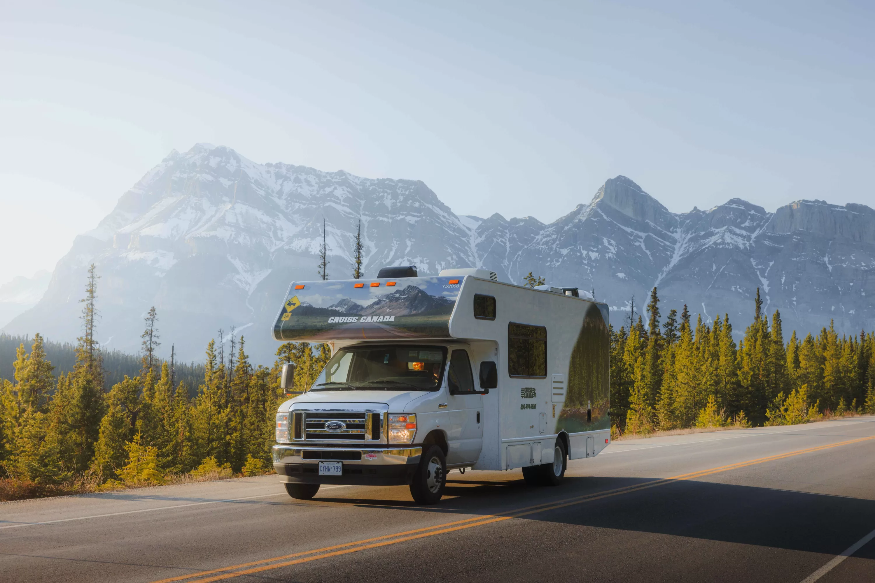 Een Cruise Canada camper op een weg met besneeuwde bergen op de achtergrond